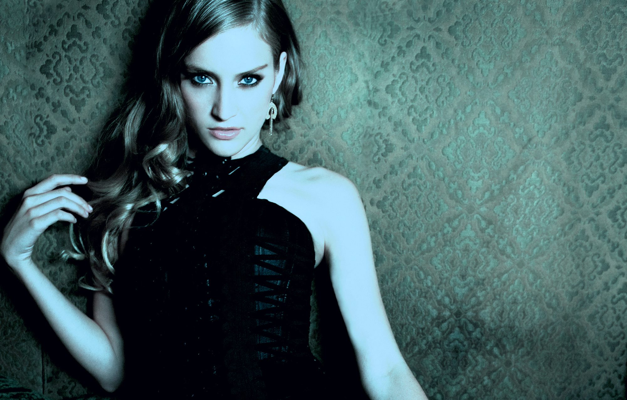 Woman leaning against wall with hand touching shoulder.